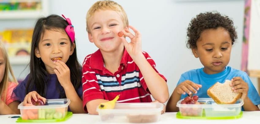 三个孩子坐在一桌，微笑着吃着健康的食物